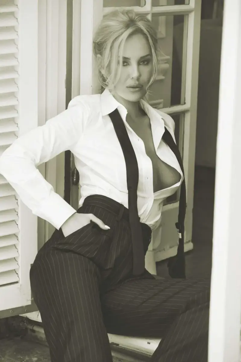 Black-and-white portrait of Katherine Taylor leaning in a shuttered doorway in a white shirt, suspenders, and pinstripe trousers